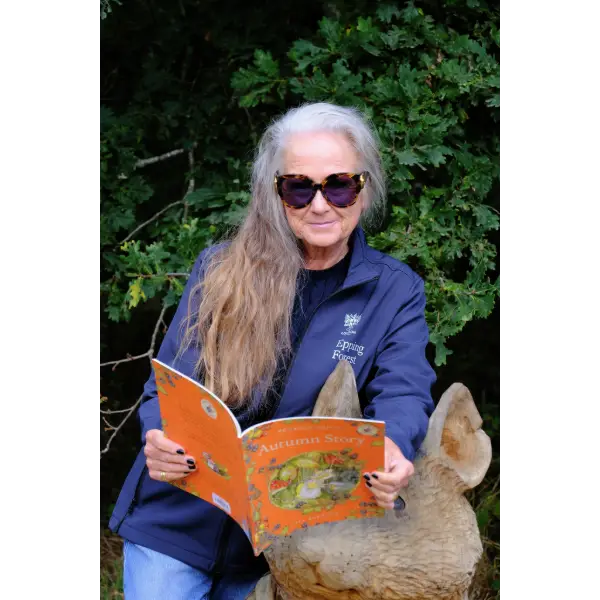 Chair, Caroline Haines, reading Brambly Hedge Autumn Story by wooden mouse sculpture.