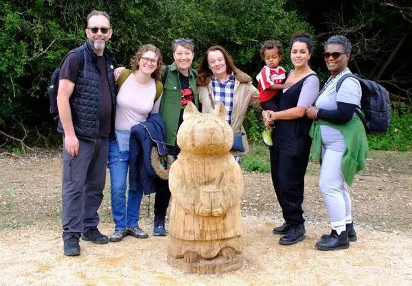 Group of people around a carved oak sculpture of a Brambly Hedge mouse character.