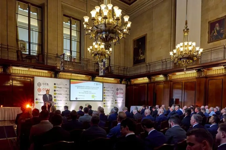 Formal awards ceremony in an ornate hall, with a speaker at a podium addressing an audience seated in rows.