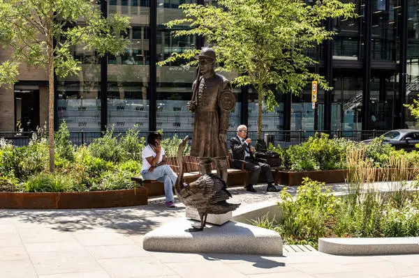 two people sitting on benches at Little Trinity Lane, with a bronze statue of of a man and swan in front of them.